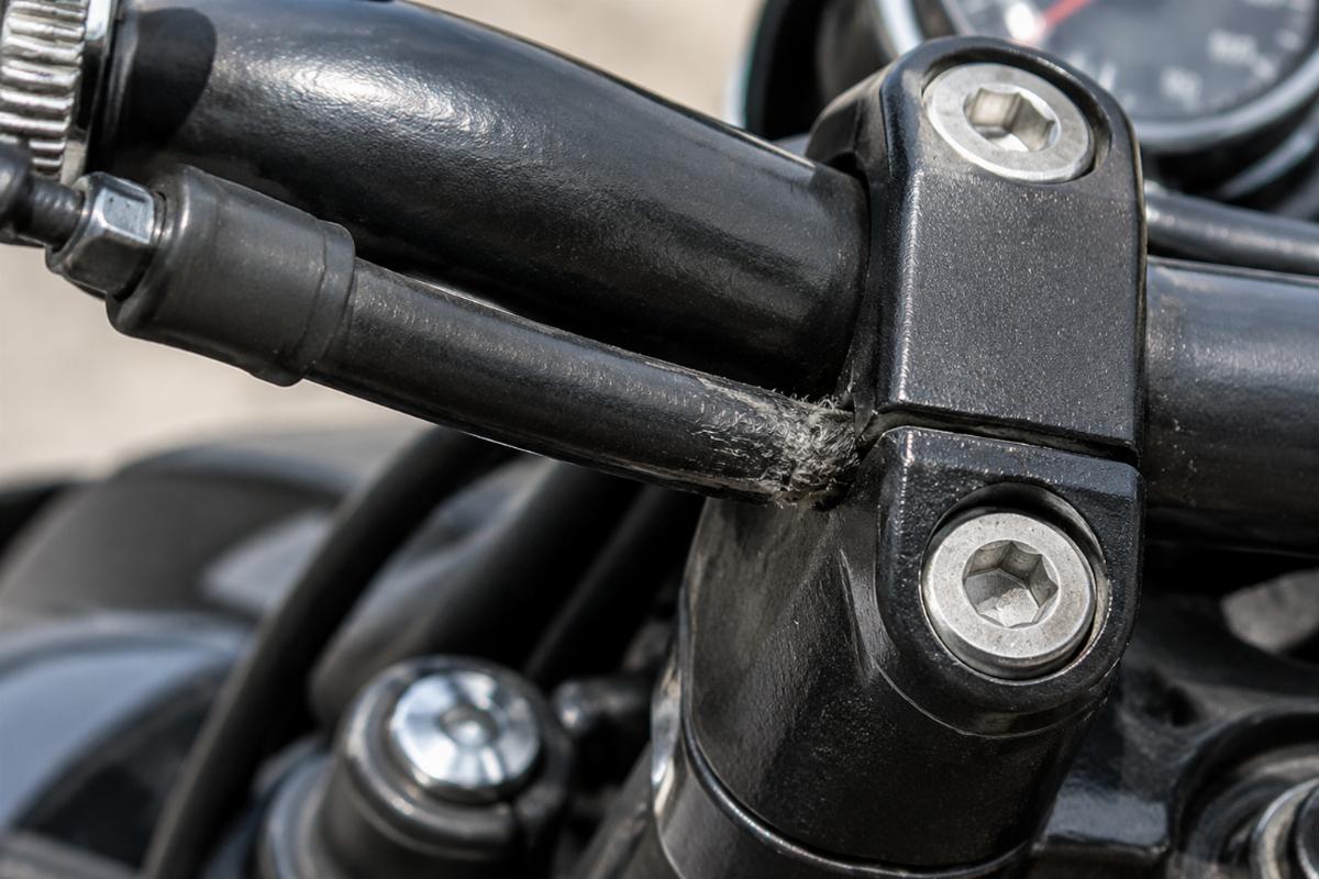 Motorcycle throttle cable chafing against a riser clamp showing worn insulation